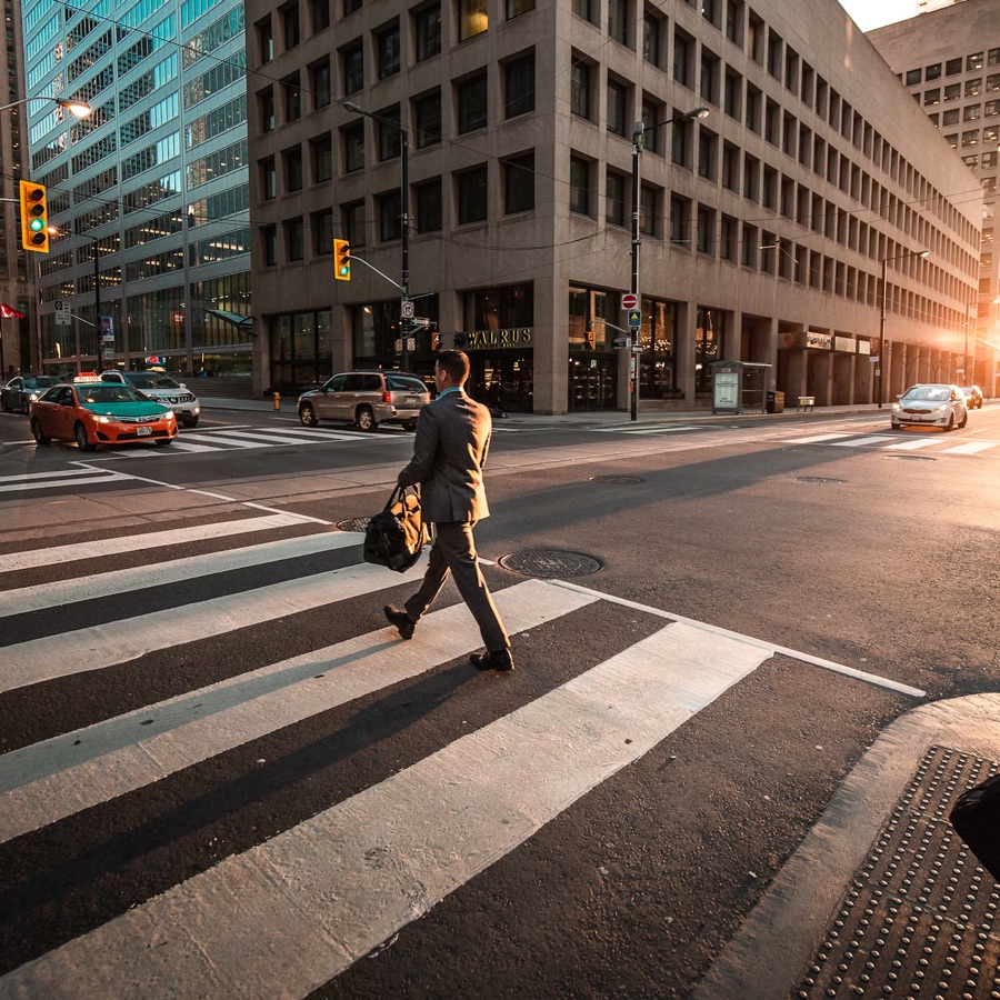 A businessman crossing a city street at sunrise