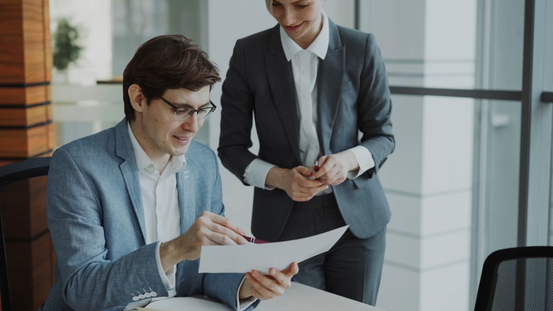 A man at a desk reviewing a document while a colleague stands beside him