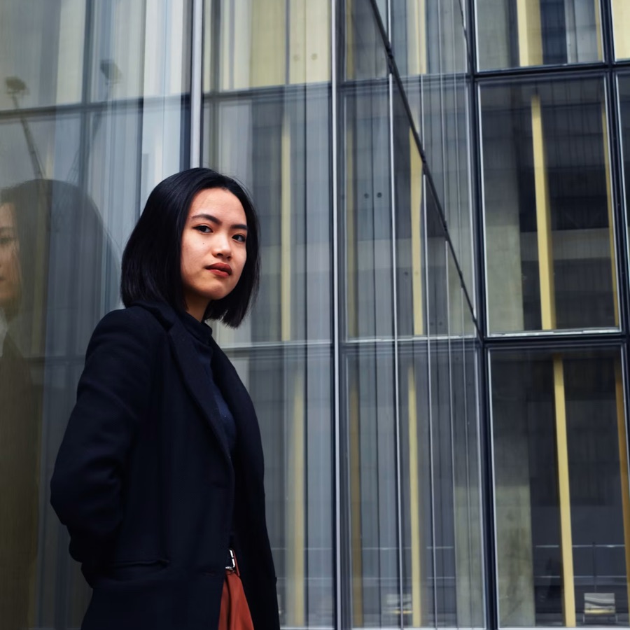 A woman in a dark coat standing beside a glass office facade