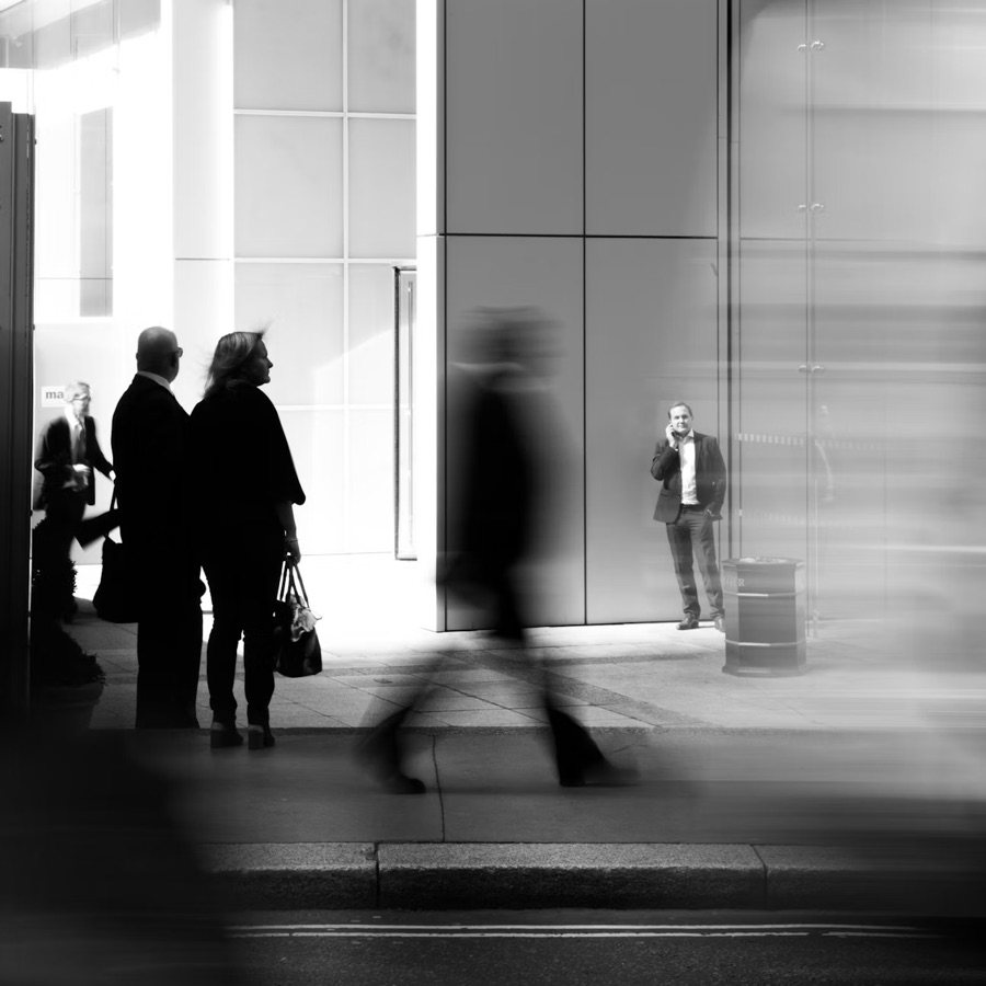 A blurred figure walking past people standing still on a city pavement